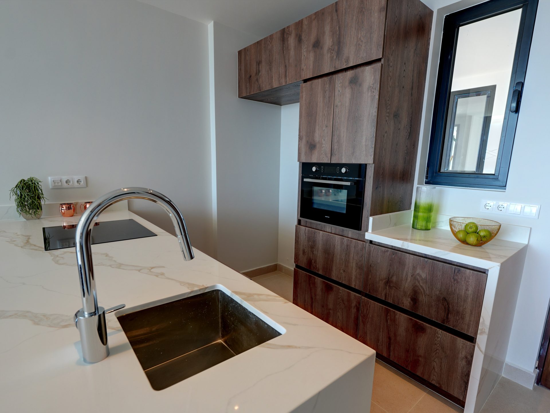 Moderne keuken met marmeren aanrechtblad, chroomkraan, ingebouwde oven, houten kasten en groene appels in een schaal, passend bij de Majestic Apartments & Hotel in Curaçao.