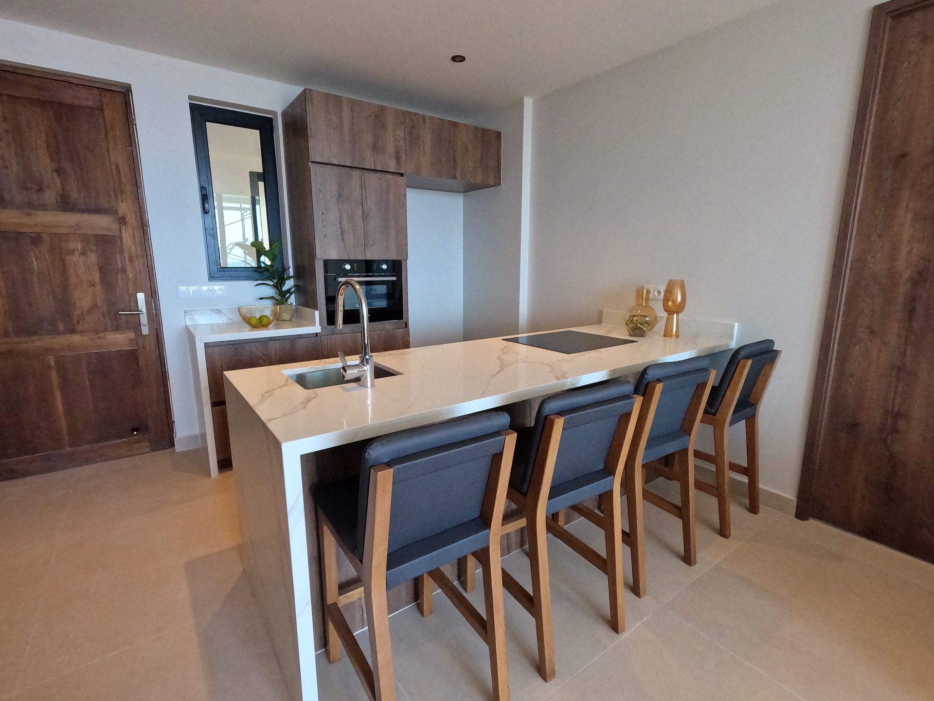 Moderne keuken met een marmeren aanrechtblad, houten kasten, en barstoelen, benadrukt de eigentijdse stijl van de Majestic Apartments & Hotel in Curaçao.