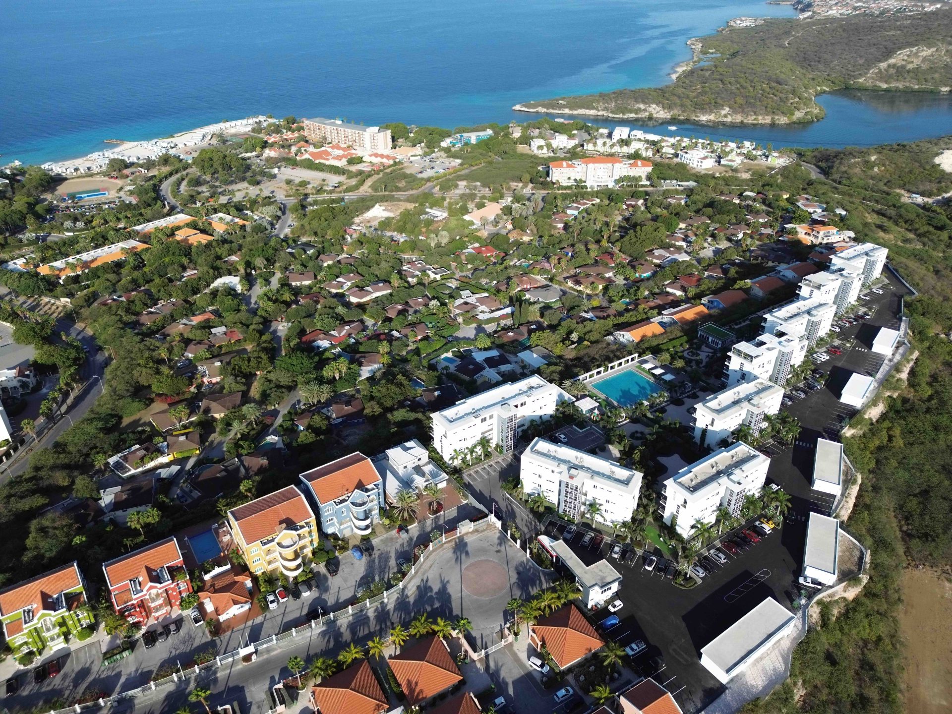 Aerial view of Grand View Residences with colorful buildings, lush greenery, and a coastline in the background, highlighting the residential area near the beach.