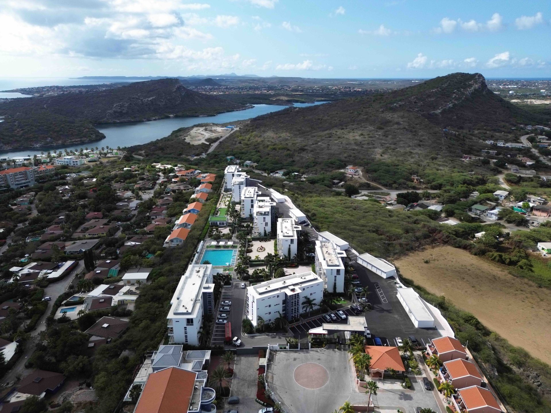 Aerial view of Grand View Residences and surrounding area, showcasing residential buildings, a swimming pool, and nearby hills in a coastal setting.