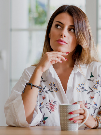 A woman sitting at the kitchen table with a drink, thinking.