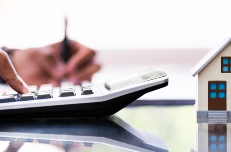 Close-up of a person typing on a calculator with a miniature house next to it