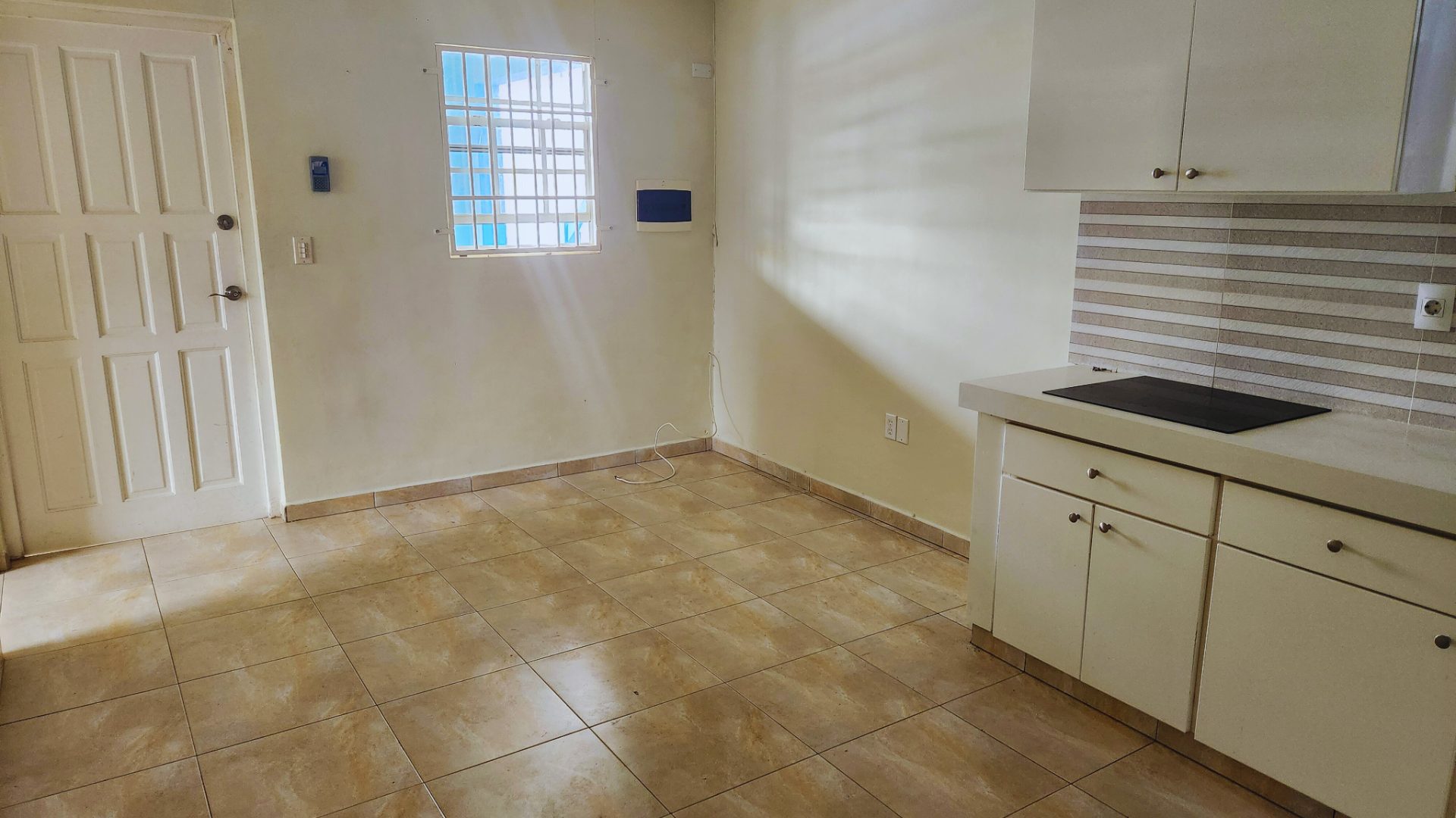 One-bedroom apartment interior with tiled floor, kitchen area featuring a countertop and stove, door leading outside, and window allowing natural light.