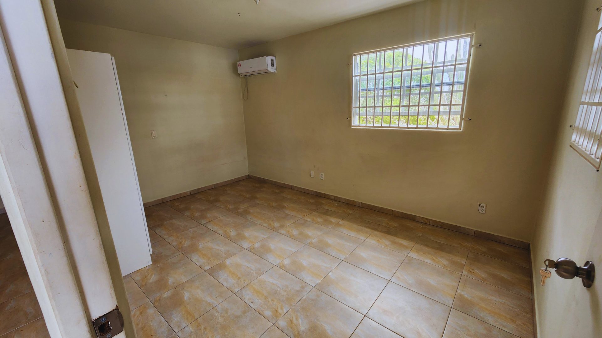 One-bedroom rental apartment interior with tiled floor, air conditioning unit, and window providing natural light, suitable for potential tenants in Abrahamsz.