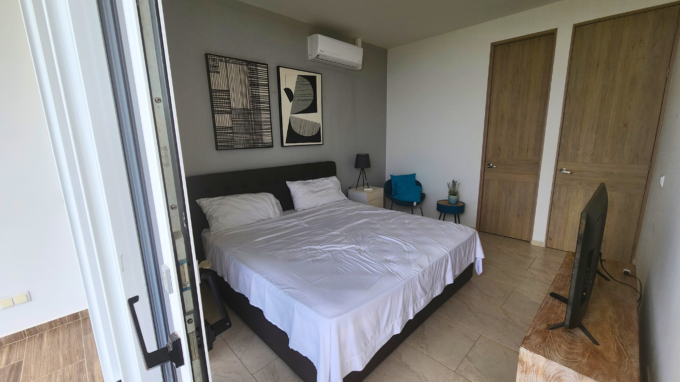 Modern bedroom interior with a king-sized bed, minimalist decor, wall art, air conditioning unit, and a TV on a wooden stand, showcasing a cozy and stylish living space.