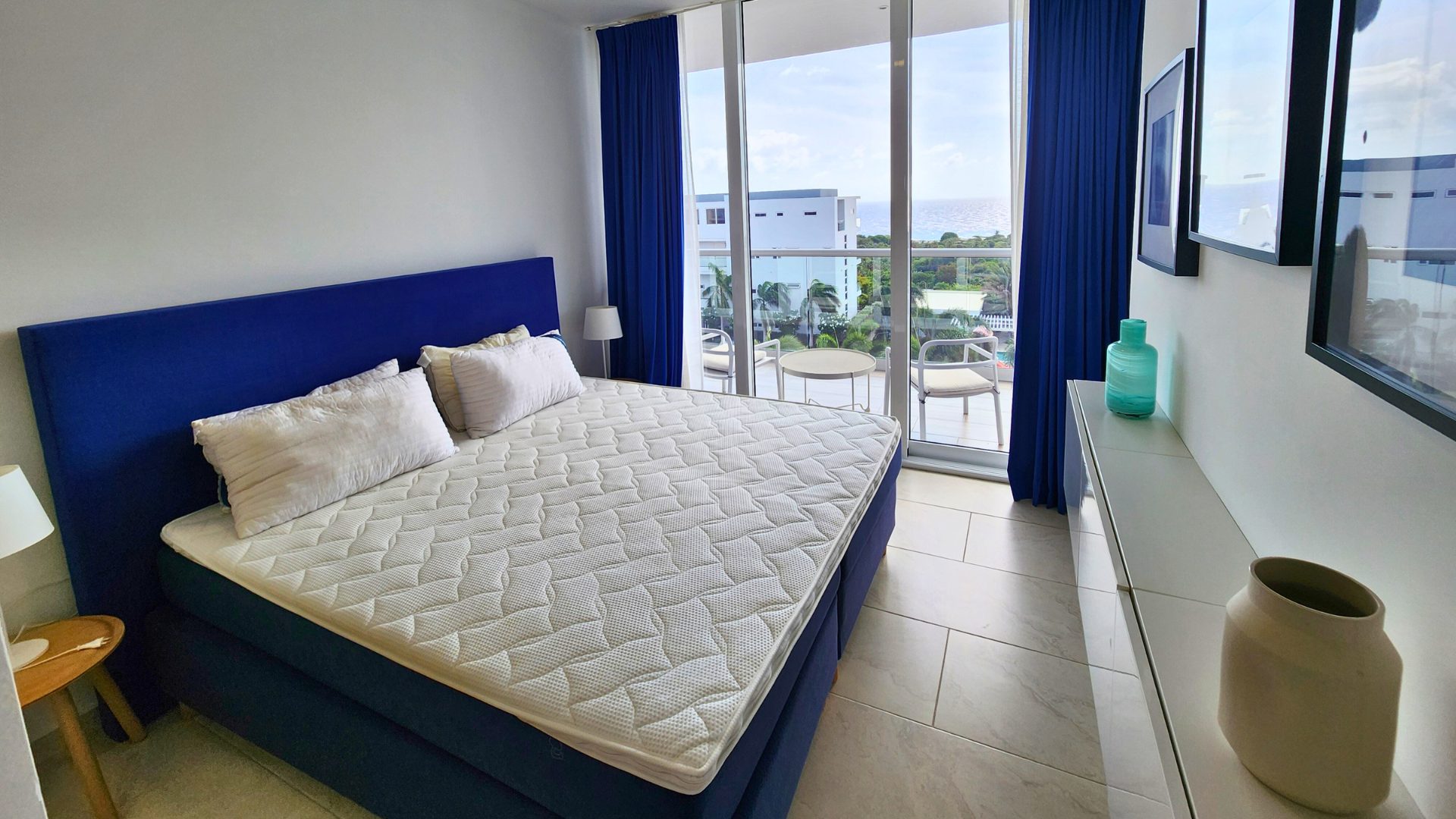 Luxury bedroom in Grand View Residences Penthouse C11, featuring a blue bed with white bedding, large windows with ocean view, and modern decor elements.
