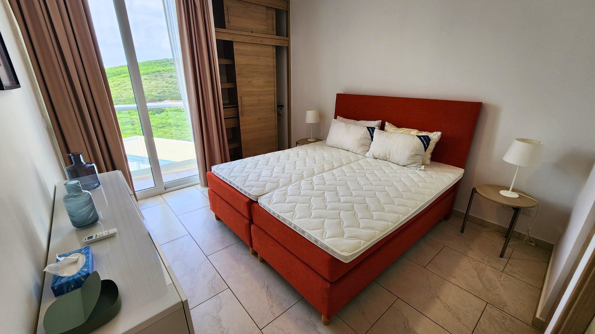 Slaapkamer in luxe penthouse C11 met oranje bed, moderne decoratie, en uitzicht op groene omgeving in Piscadera, Curaçao.