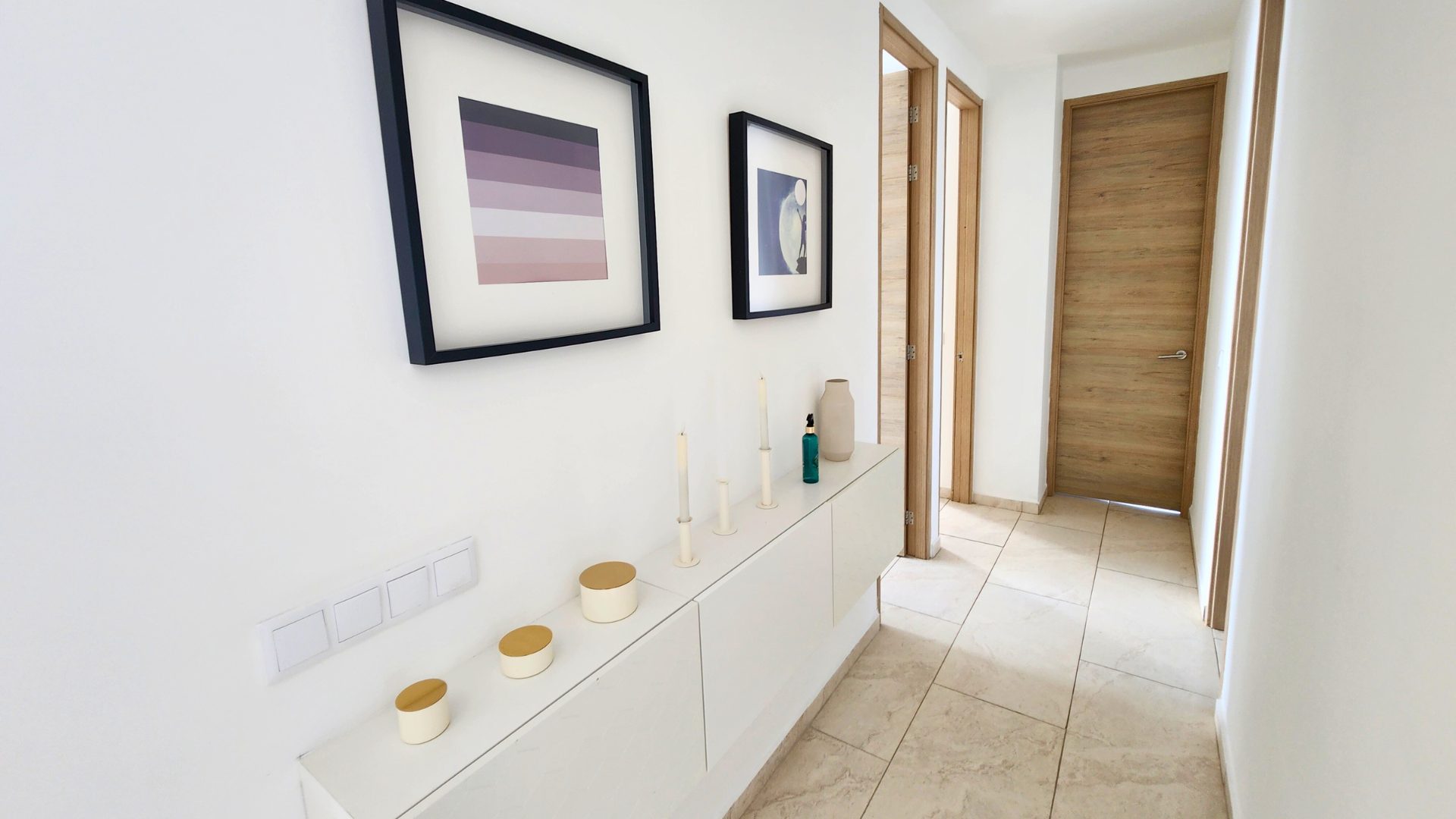Modern hallway decor with framed abstract art, candles, and a vase, showcasing the elegant interior design of the Grand View Residences Penthouse C11 in Piscadera, Curaçao.