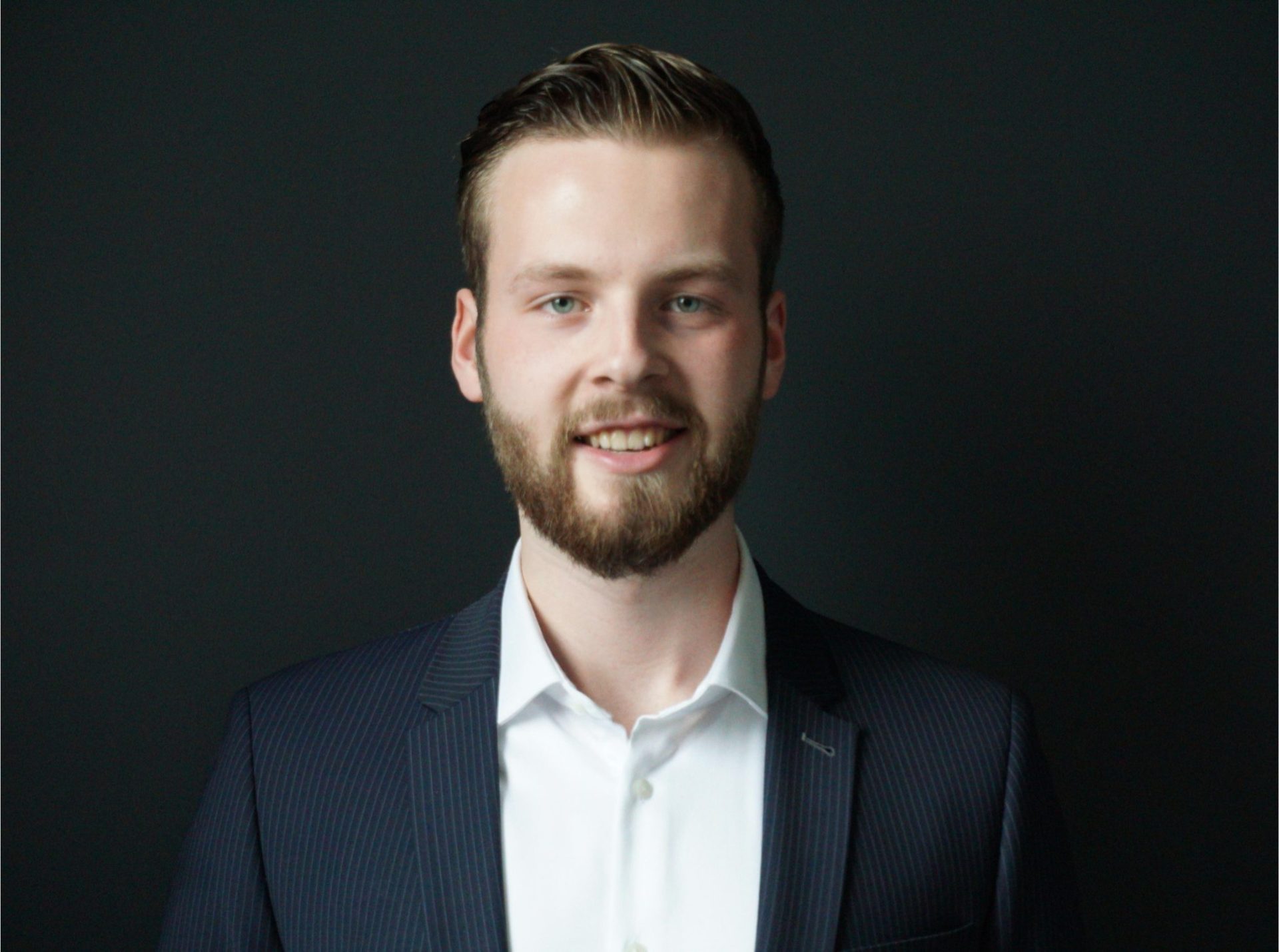 Sales agent Antonie Thijsen in a professional suit, smiling against a dark background, representing New Winds Realty.