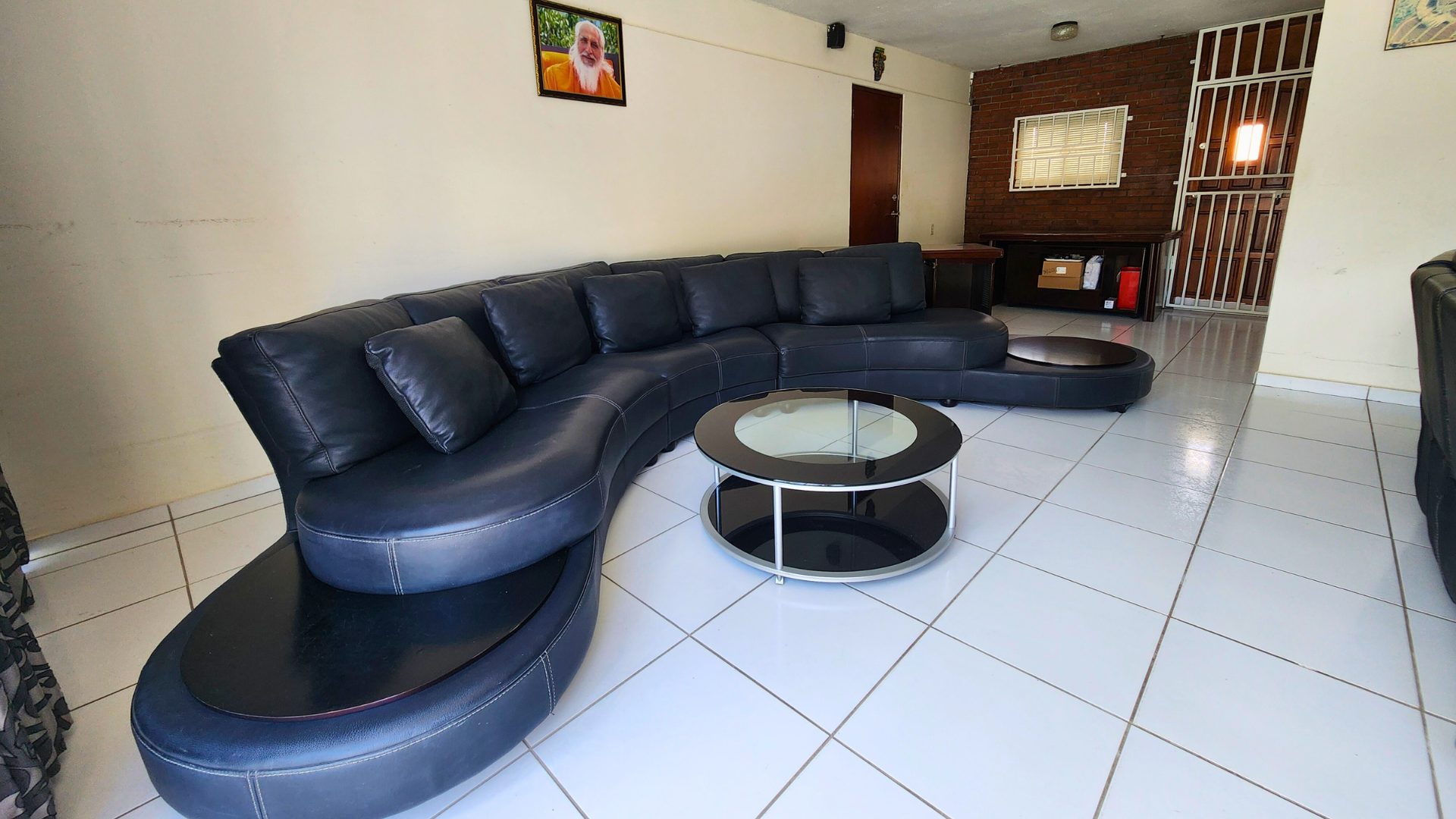 Zwarte leren bank in een woonkamer met ronde salontafel en schilderij aan de muur, geschikt voor gezinsleven in Curaçao.