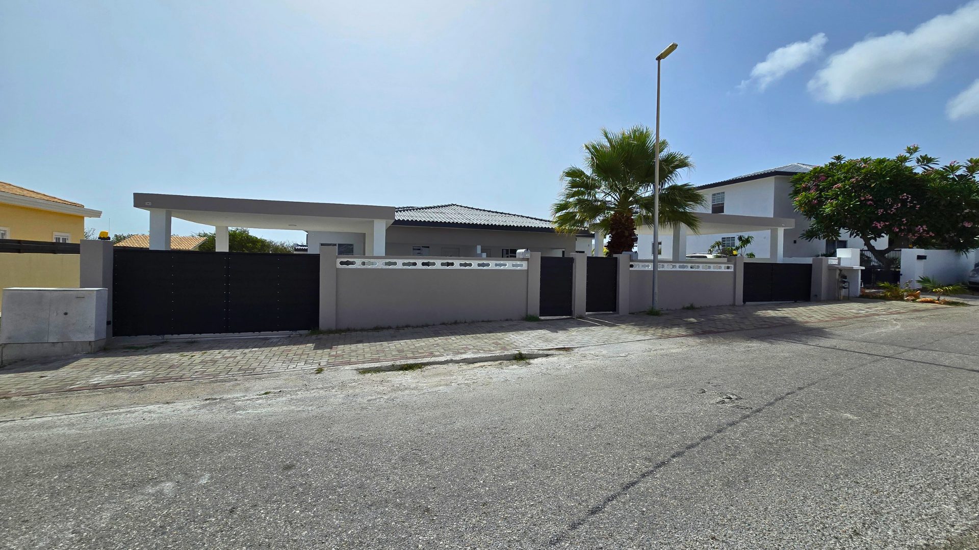 Moderne duplex woning met zwarte poort en tropische beplanting, gelegen in een rustige woonwijk van Curaçao, ideaal voor verhuur.