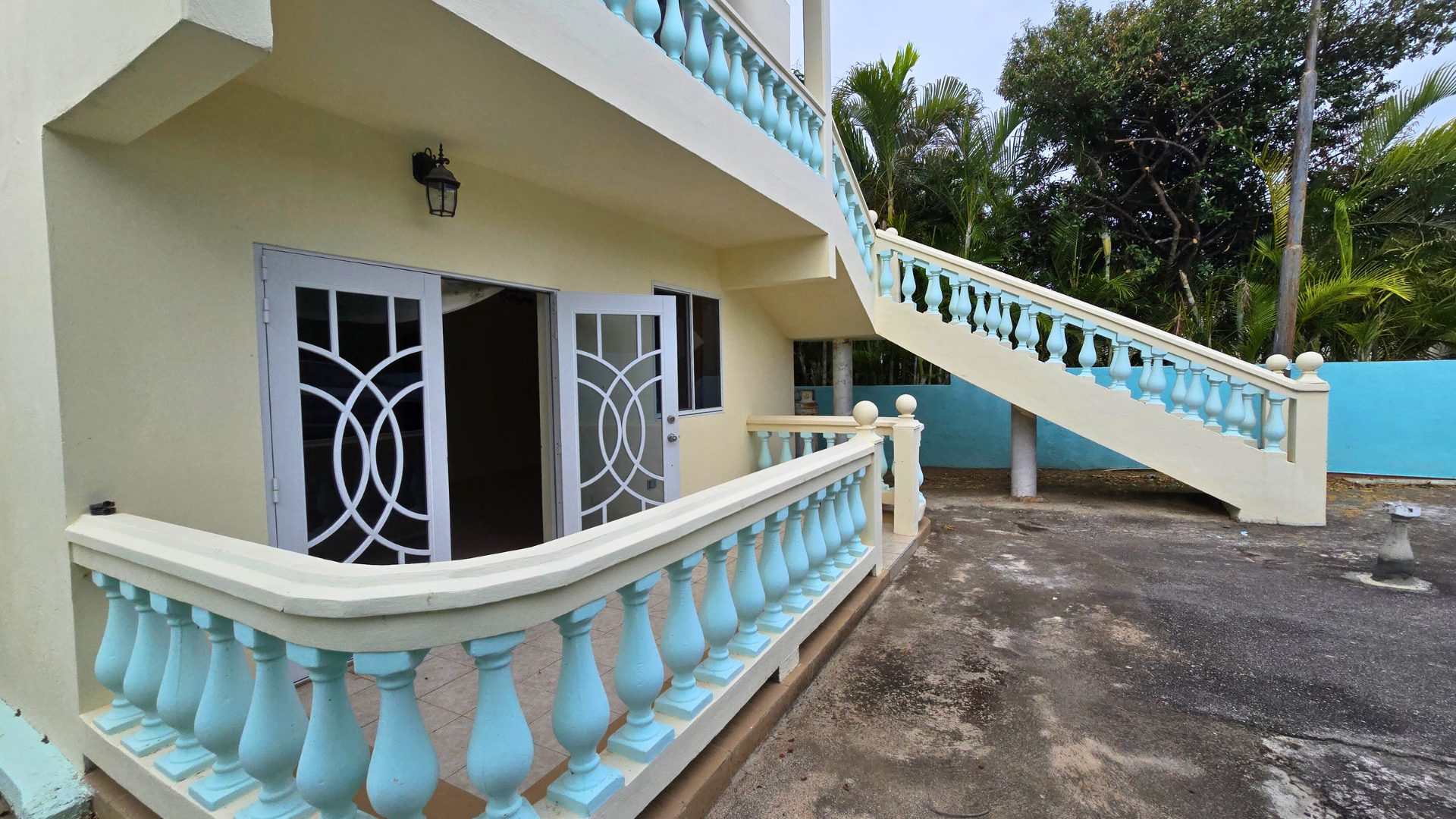 Veranda with decorative railing and staircase leading to a rental property in Curaçao, showcasing architectural features and surrounding greenery.