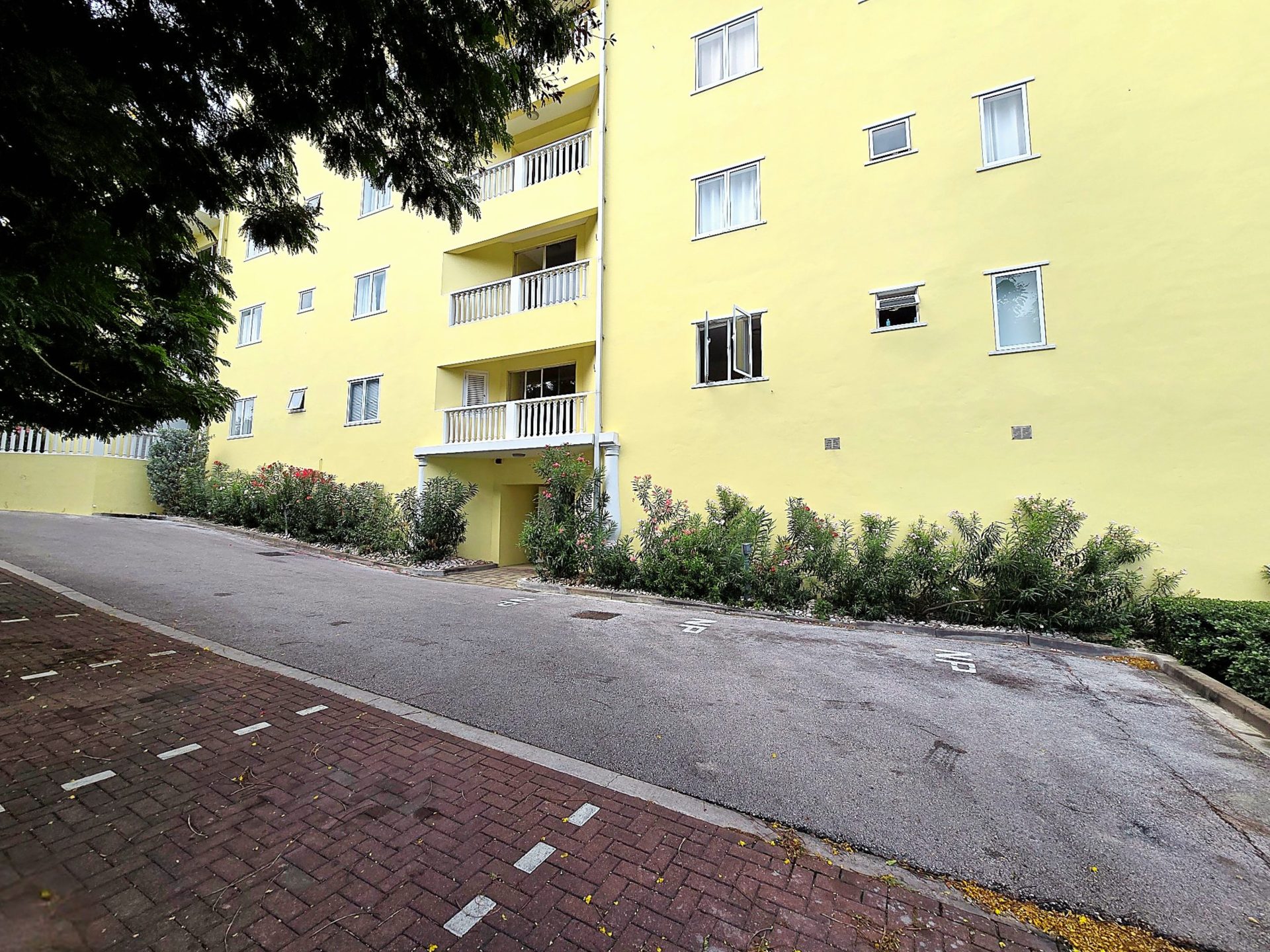 For rent Blue Bay 1-bedroom apartment - side exterior view with parking spaces and yellow building facade.