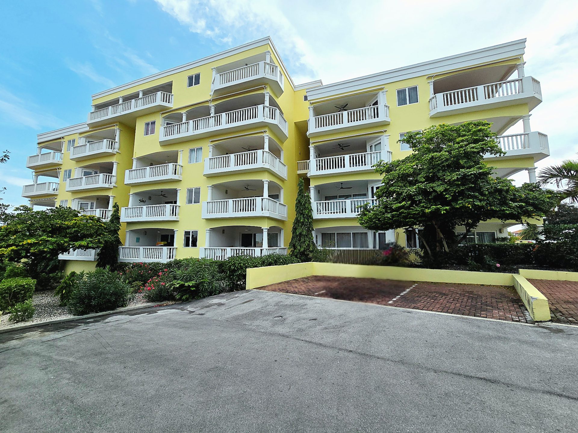 For rent Blue Bay 1-bedroom apartment - exterior view of yellow apartment building with paved parking are