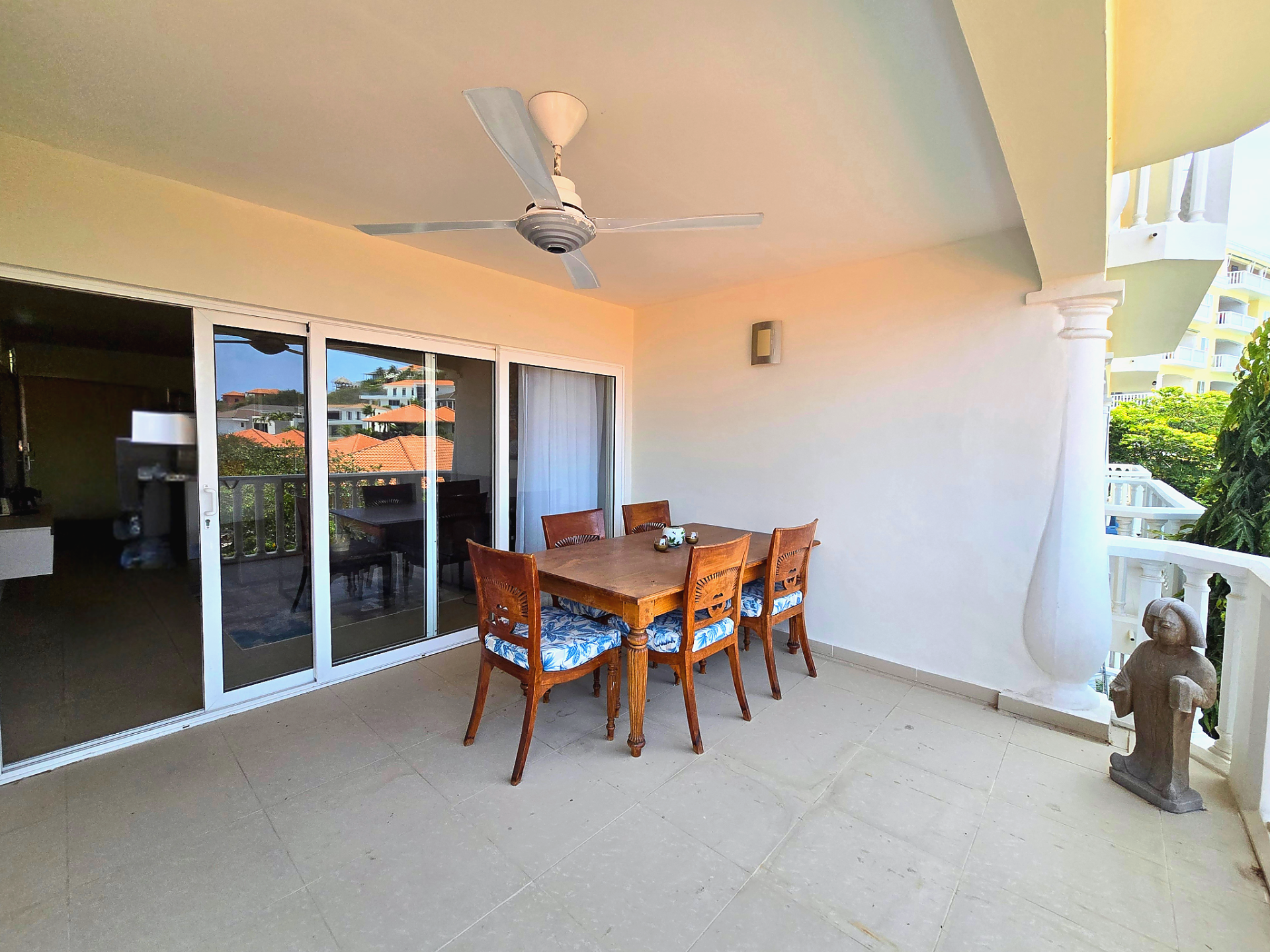 For rent Blue Bay 1-bedroom apartment - covered balcony with outdoor dining set, ceiling fan, and sliding glass doors.